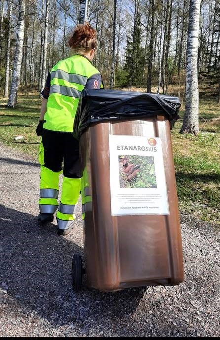 Huomiovaatteisiin pukeutunut nainen vetää poispäin roskispönttöä, jonka kyljessä lukee etenaroskis.