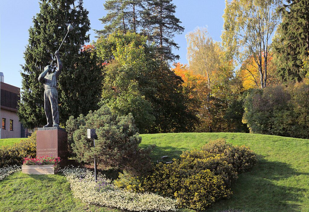 Lasinpuhaltajapatsas Lasinpuhaltajan puistossa, puustoa patsaan taustalla.