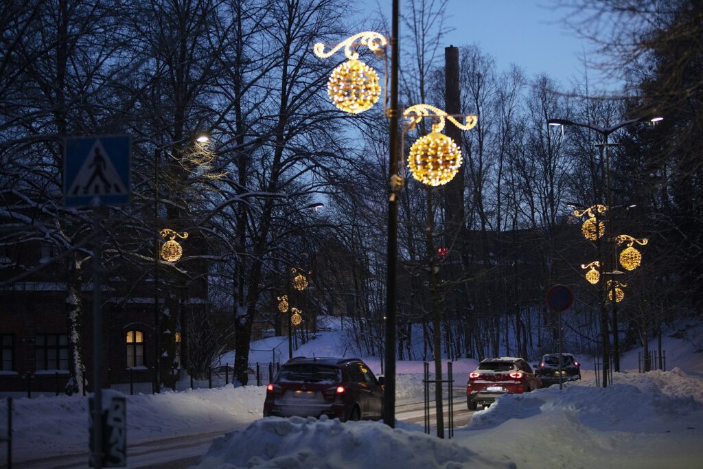 Tummansinisessä iltahämärässä pallonmuotoiset jouluvalot autotien varrella pylväissä.